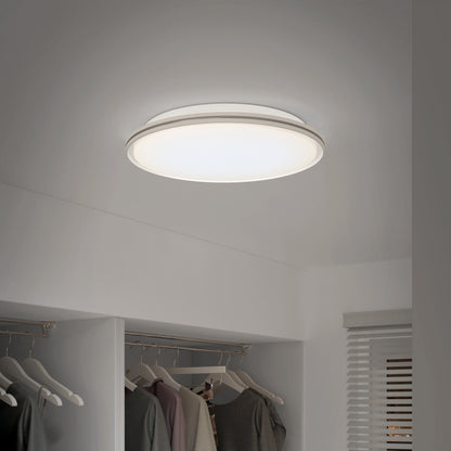 The Artika Astrid 16.5 in. LED flush mount light (5 CCT, remote included) brightens a minimal, tidy closet with hanging clothes and neutral walls, casting soft light near a window with closed blinds.