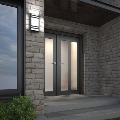 Modern double glass doors with frosted panels set in a stone wall, illuminated by the Artika Glowbox 3 indoor-outdoor LED wall light above wide gray steps, with greenery visible in the corner.