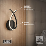 Modern wall-mounted light with a matte black finish and curved integrated LED design is installed beside a upholstered bed. Text highlights its energy efficiency and 3-year warranty; no bulbs are required.