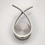 A modern, sculptural LED table lamp with two curved, intersecting metal arms forming an elegant loop above a circular base, set against a white background.