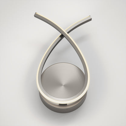 The Gamma modern LED wall sconce 5 CCT by Artika features a sculptural design with two curved metallic arms crossing at the top to form a loop, integrated LED strips along the inner edges, and is set on a round base against a plain white background.