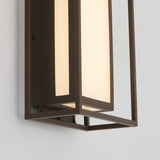 A close-up of a modern wall-mounted light fixture with a rectangular frame and frosted glass, emitting a warm glow against a white wall.