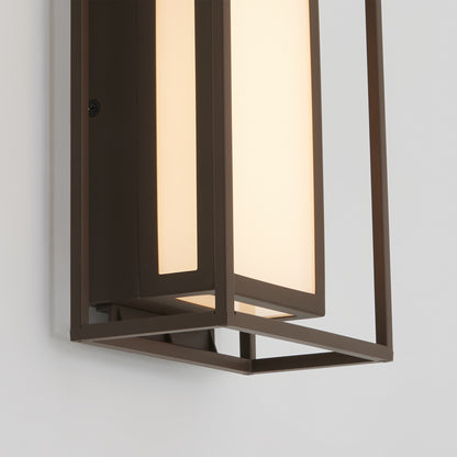 A close-up of the Artika Ghost indoor-outdoor LED wall light features a rectangular bronze frame and frosted glass panel, casting a soft, warm glow against a white wall.