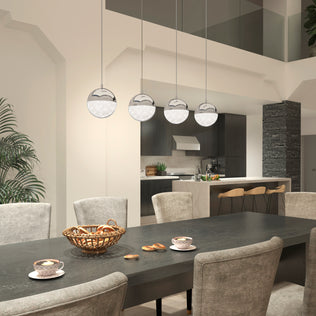 A modern dining area features a dark table, upholstered chairs, and pastries under the Artika Sparkle 4-light LED pendant. Teacups sit on the table, with a chic kitchen and bar stools visible in the background.
