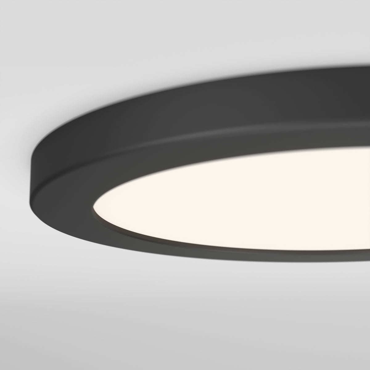 Close-up view of a modern, round, black ceiling light fixture with a smooth, illuminated white surface against a light gray ceiling background.