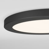 Close-up view of a modern, round, black ceiling light fixture with a smooth, illuminated white surface against a light gray ceiling background.