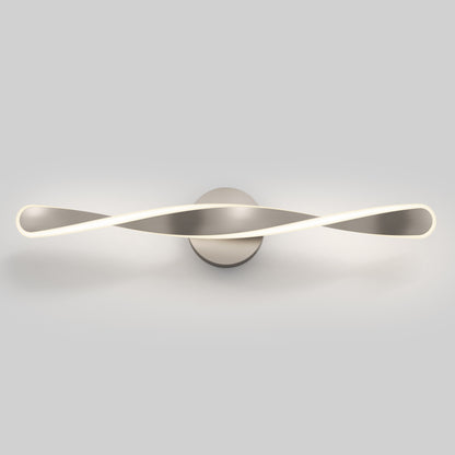 The Artika Finley LED modern bathroom vanity light features a twisted, ribbon-like brushed metal design and emits a soft white glow. It is wall-mounted with 3 selectable color temperatures. Shown against a plain light gray background.