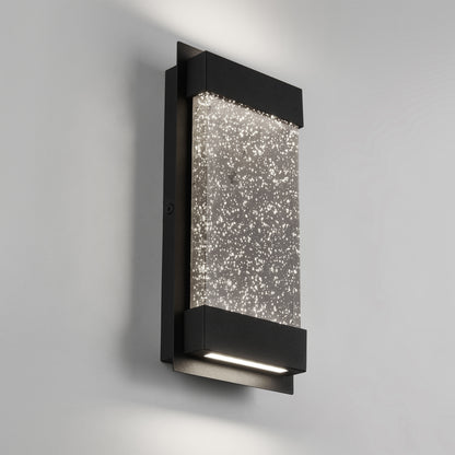 The Artika Essence Glow Box indoor-outdoor LED wall light features a modern rectangular black frame and textured glass panel, casting a sparkling glow on any plain light gray wall.