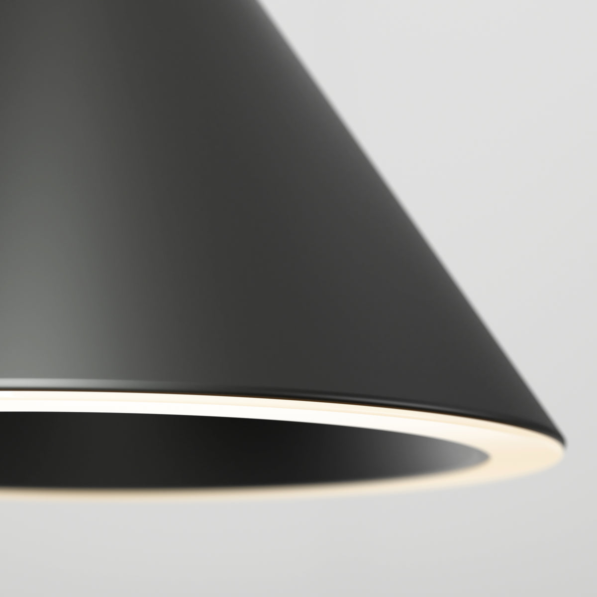 Close-up of a modern, black, conical lampshade with a glowing white inner edge, set against a plain light gray background.