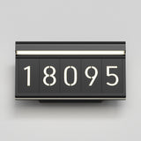 A modern black house number sign displays the numbers “18095” in large, illuminated white digits against a light gray background.