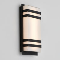 The Artika Glowbox 3 indoor-outdoor LED wall light features a modern rectangular design with a frosted glass shade framed by three horizontal black metal bands, mounted on a black backplate against a light gray wall.