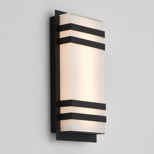 The Artika Glowbox 3 indoor-outdoor LED wall light features a modern rectangular design with a frosted glass shade framed by three horizontal black metal bands, mounted on a black backplate against a light gray wall.
