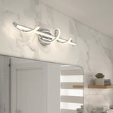 A modern bathroom features a chrome and LED swirl vanity light above a mirror, set against white marble-patterned tile walls. Floating wooden shelves with decor are visible to the right.