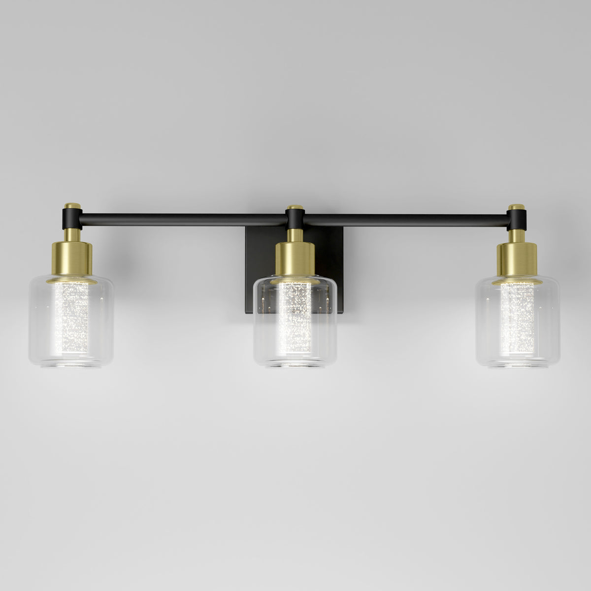 A modern wall-mounted light fixture with three cylindrical glass shades, each containing a textured inner cylinder. The fixture features black and gold accents against a plain light gray background.