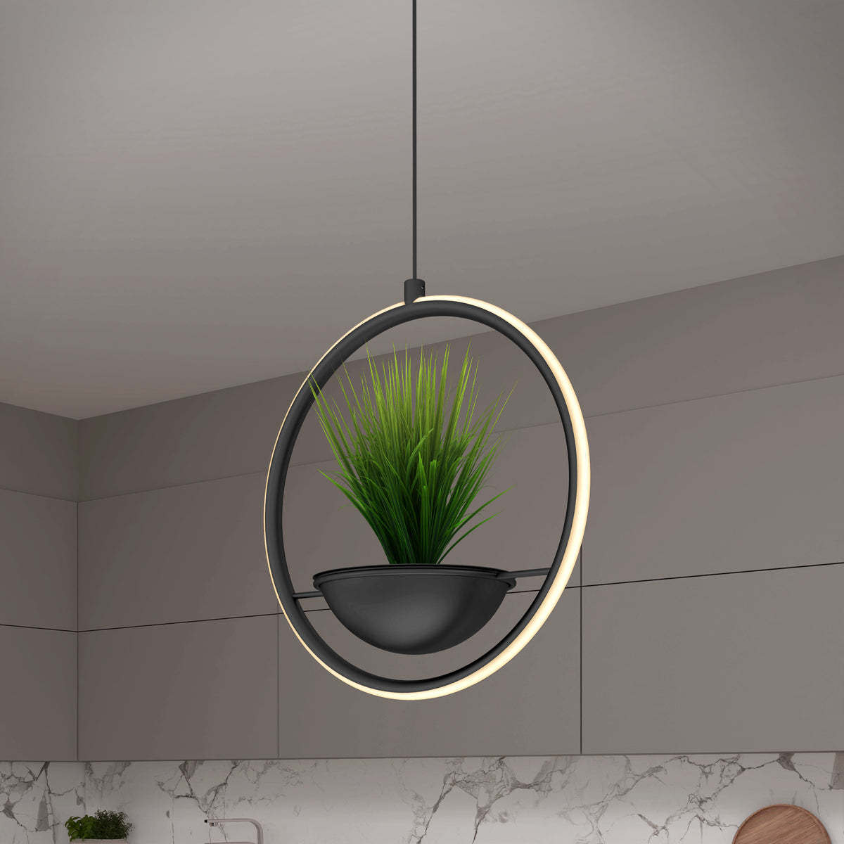 A modern pendant light with a circular LED frame surrounds a small green potted plant in a black holder, suspended from the ceiling in a contemporary kitchen with gray cabinets and a marble backsplash.