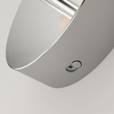 Close-up of a sleek, modern metallic object with a smooth, curved surface and a small round button on its side, set against a plain light background.