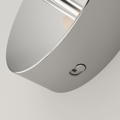 Close-up of a sleek, modern metallic object with a smooth, curved surface and a small round button on its side, set against a plain light background.