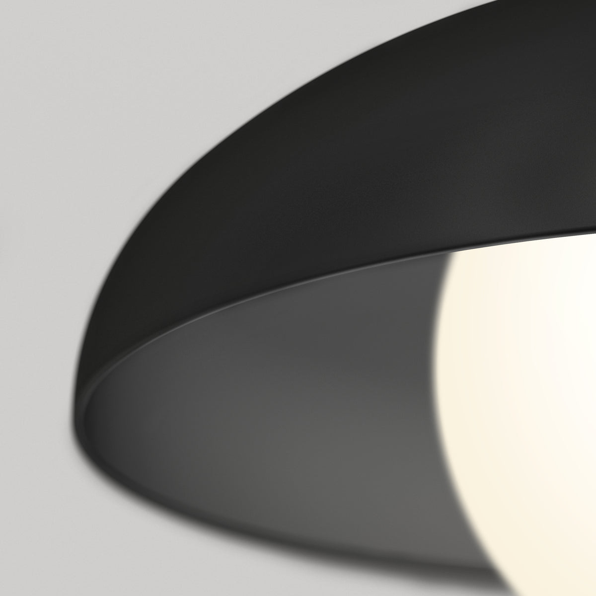 Close-up of a modern black lampshade with a glowing white light bulb partially visible, set against a light gray background.