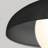 Close-up of a modern black lampshade with a glowing white light bulb partially visible, set against a light gray background.