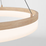 Close-up of a modern circular pendant light with a wooden rim and a glowing white diffuser, suspended by metal cables against a plain light background.