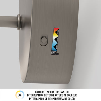 Close-up of the Artika Finley LED modern bathroom vanity light 3 CCT, showing a metallic fixture with a button and a color temperature switch label with white, yellow, and blue segments. COLOUR TEMPERATURE SWITCH appears in three languages below.