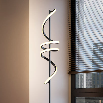The Artika Coda modern LED floor lamp 5CCT, featuring spiraling dimmable light tubes, is positioned near a window with partially open blinds, offering views of tall city buildings outside.