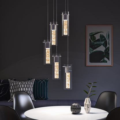 Modern dining room featuring an Artika Essence 5-light LED pendant above a round white table with black chairs. A dark sofa with patterned cushions and a framed leafy art print complete the background.
