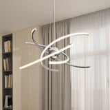 A modern, abstract LED chandelier with curved metal arms hangs from the ceiling in a bright room with beige cabinets, bookshelves, and sheer curtains covering large windows.