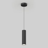 A modern black pendant light with a cylindrical, ribbed shade hangs from the ceiling by a thin cord against a plain light gray background.