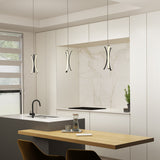 A modern kitchen with white cabinets, marble backsplash, and three sculptural pendant lights. A wooden table with a glass carafe and cups sits near a gray island with a black faucet. A small potted plant is by the backsplash.
