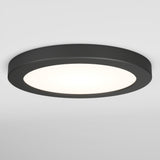 A round, black flush-mounted ceiling light with a white illuminated center, installed on a plain white ceiling.