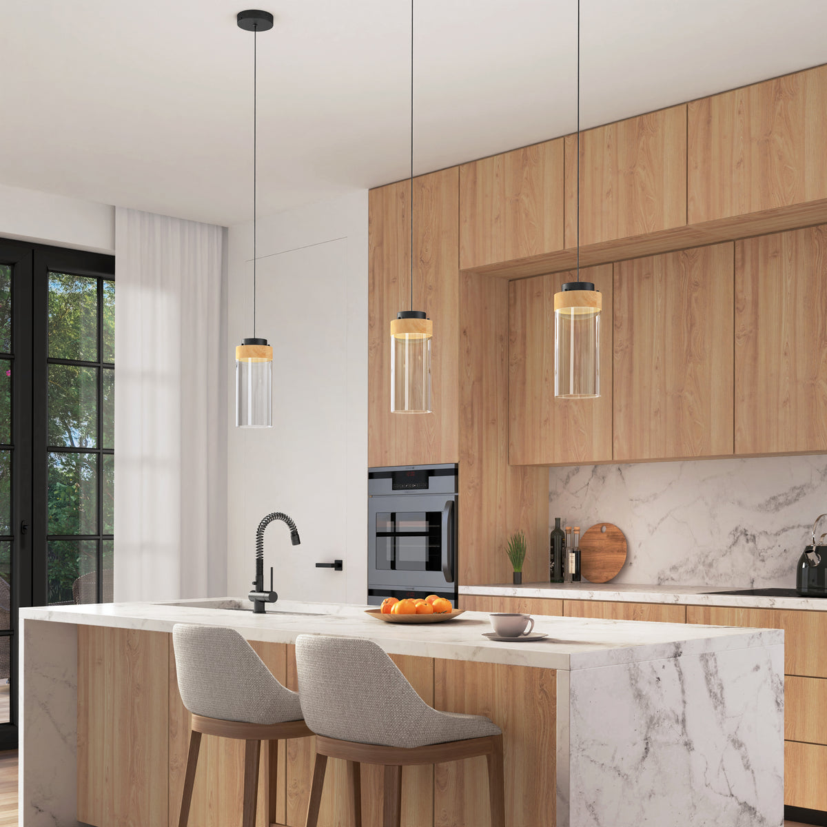 Modern kitchen with light wood cabinets, marble countertops, and island with two beige upholstered stools. Three pendant lights hang above the island. Built-in oven, sink, and fruit bowl are visible. Large window lets in natural light.