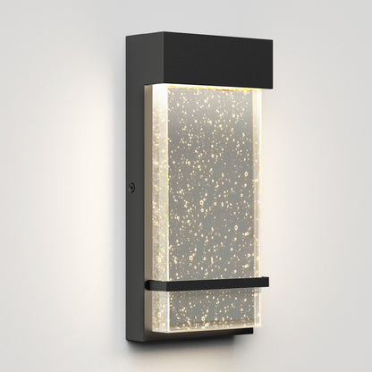 The Artika Skyler indoor-outdoor LED wall light features a modern rectangular black frame and a frosted bubble glass panel, emitting softly diffused warm white light.