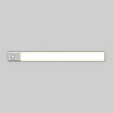 A slim, rectangular LED light bar with a metallic end cap featuring a button and three small icons, mounted on a plain light gray wall.