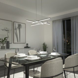 A modern dining room features a glass table for four, upholstered chairs, abstract wall art, plants, large windows with sheer white curtains, and the Artika Grid modern LED pendant light 5 CCT illuminating the space.