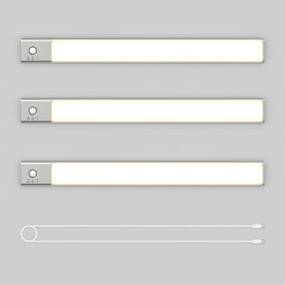 Three Artika Outline under cabinet LED light 3CCT bars with silver ends and control buttons are arranged horizontally on a light gray background. Below them lies a white USB charging cable with connectors on both ends.