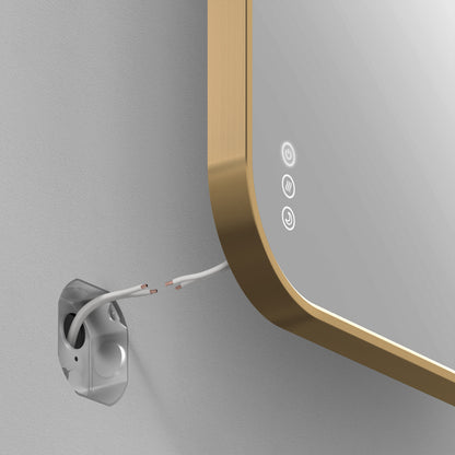 A close-up of the Artika Royce Dimmable LED Mirror, 3 CCT, shown wall-mounted with touch controls and a gold frame, installed horizontally near exposed wires from a wall outlet box.