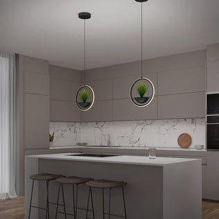 Modern kitchen with gray cabinets, marble backsplash, and island seating. Two Artika Colin LED modern planter pendant lights hang above, each featuring circular frames and small potted plants. A glass and wooden cutting board sit on the counter.