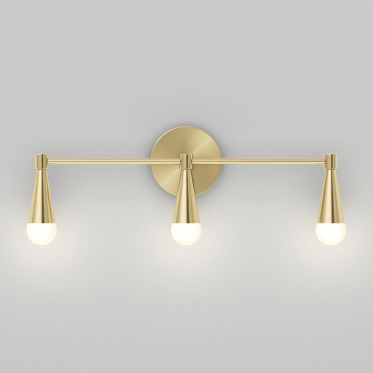 A modern wall sconce with a brushed gold finish, featuring three evenly spaced cone-shaped light fixtures, each with a round bulb, mounted on a circular backplate against a light gray wall.