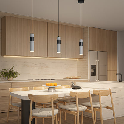 Modern kitchen with light wood cabinets, marble backsplash, and an island with a sink. Four wooden chairs surround a dining table with oranges. Above the island hang three Artika Barden 1-light LED pendant 5 CCT lights.
