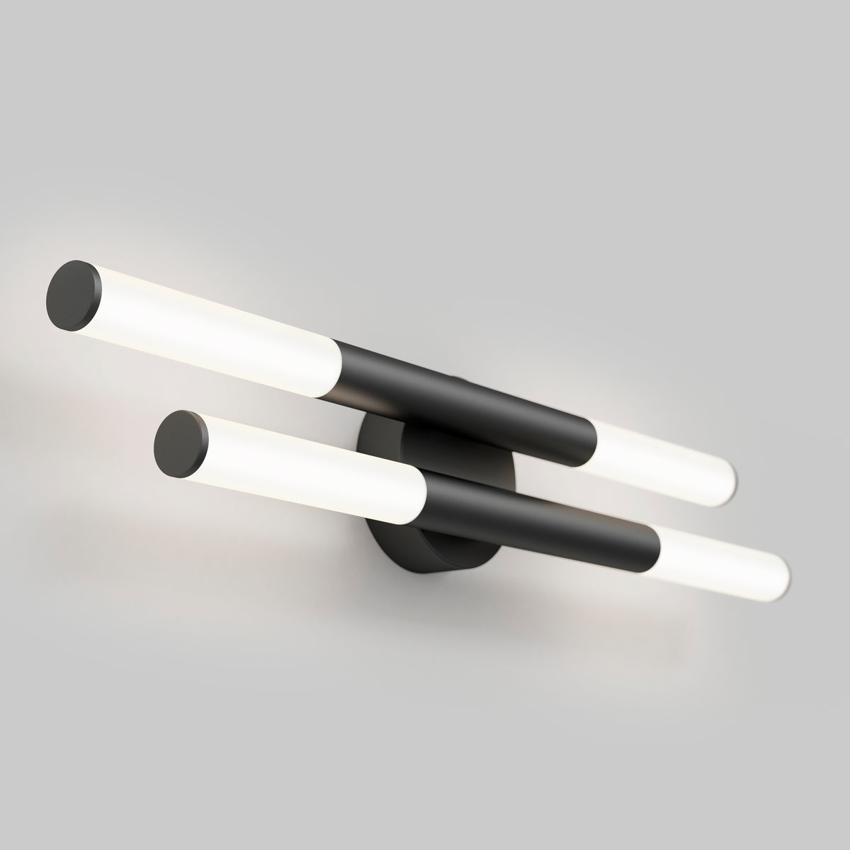 A modern wall sconce with two parallel black cylindrical bars, each with white illuminated ends, mounted on a round black base against a plain light gray background.
