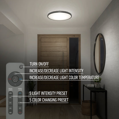 A modern hallway features the Artika Athos 21 in. LED flush mount light with remote, a wooden door, round wall mirror, and small decor table. The remote displays labeled intensity and color adjustment features.