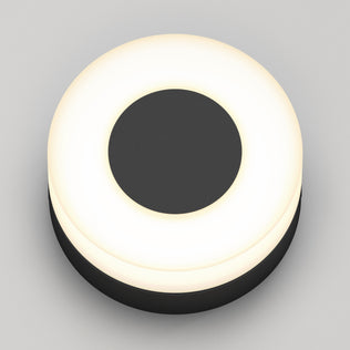 The Ludwig modern LED indoor-outdoor wall light by Artika features a minimalist round design with a black center and glowing white ring, suitable for walls or ceilings, shown against a plain light grey background.
