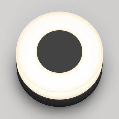 The Ludwig modern LED indoor-outdoor wall light by Artika features a minimalist round design with a black center and glowing white ring, suitable for walls or ceilings, shown against a plain light grey background.