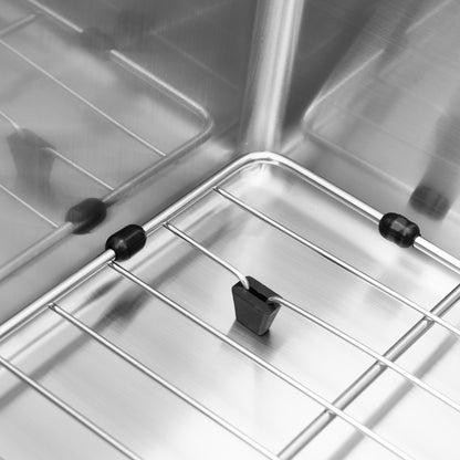 Close-up of the interior corner of the Artika Neoflow single bowl stainless steel sink, highlighting metal wire racks, black rubber or plastic stoppers, and a temperature probe clipped to the rack.