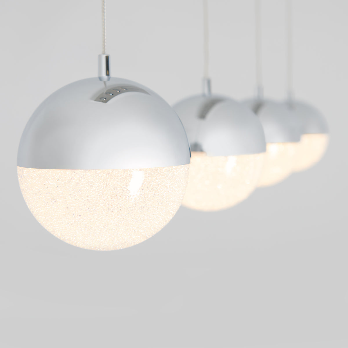 Close-up of the Artika Sparkle 4-light LED pendant, featuring shiny metallic tops and textured frosted glass bottoms, all suspended in a row against a light grey background.