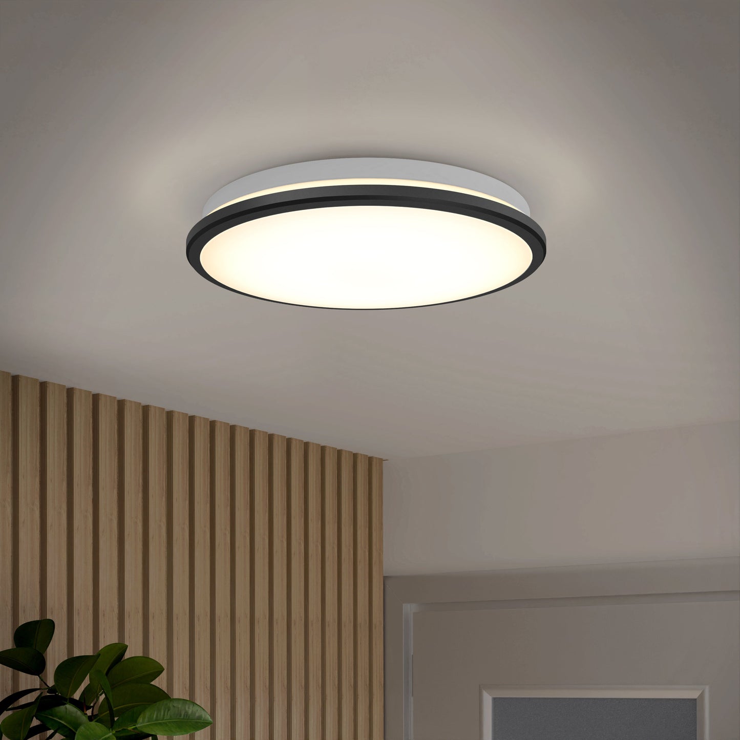 The Artika-CAN-dev Vera 13 in. LED modern flush mount light with a round matte black design softly illuminates a room featuring a wood-paneled wall, glimpses of a green plant, and a white door.