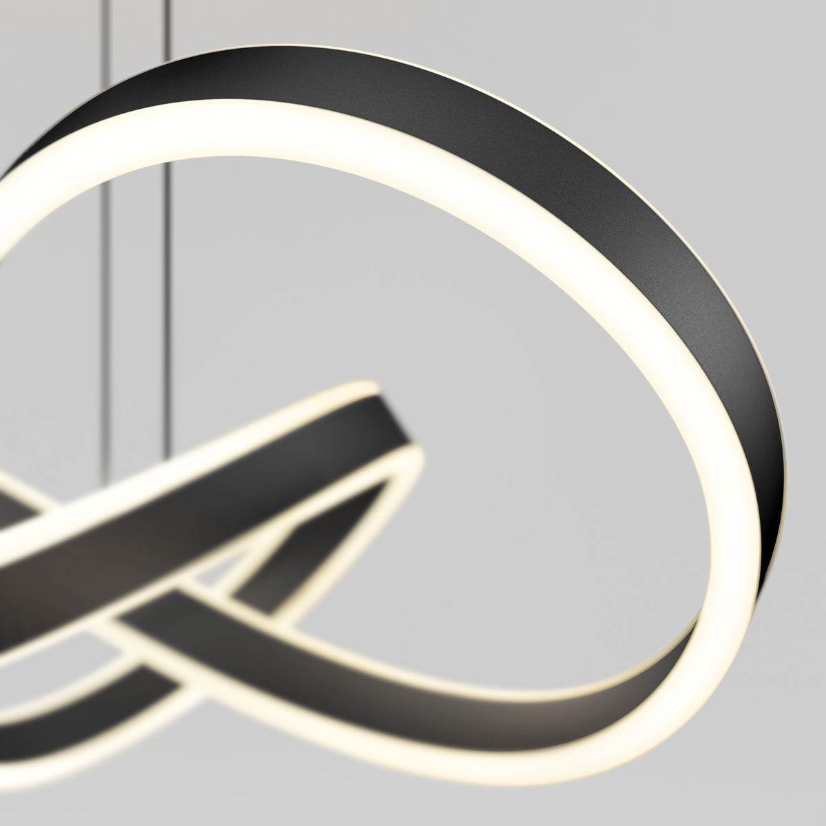 A close-up of the Artika Bolero LED pendant light 5 CCT shows two intertwined black rings emitting a soft white glow, set against a plain gray background.