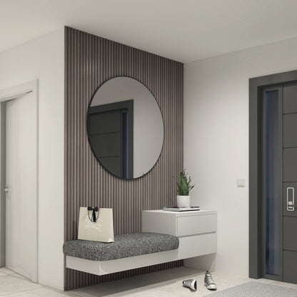 A modern entryway with a round mirror, a floating cushioned bench, a small white drawer, a potted plant, a tote bag, and a pair of sneakers on the floor next to a dark-colored door.