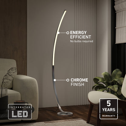 The Artika Arc LED Floor Lamp, featuring a modern arched design and chrome finish, stands beside a sofa. Its integrated LED is energy-efficient and dimmable, requires no bulbs, and comes with a 5-year warranty.